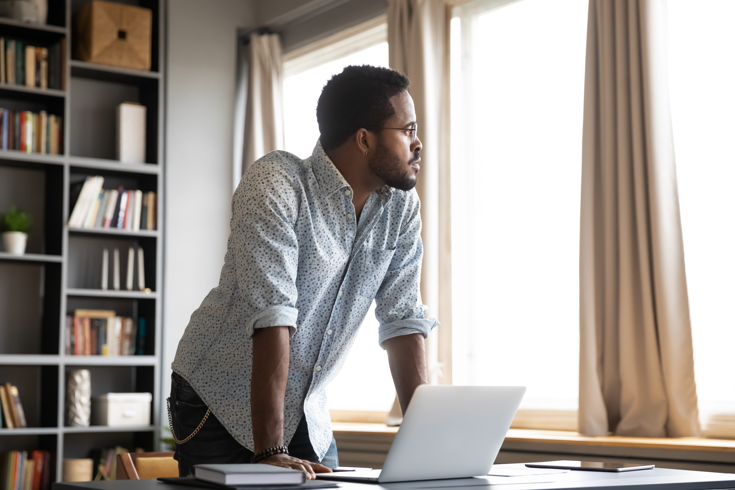 Thoughtful african american businessman leaning on table, looking away.